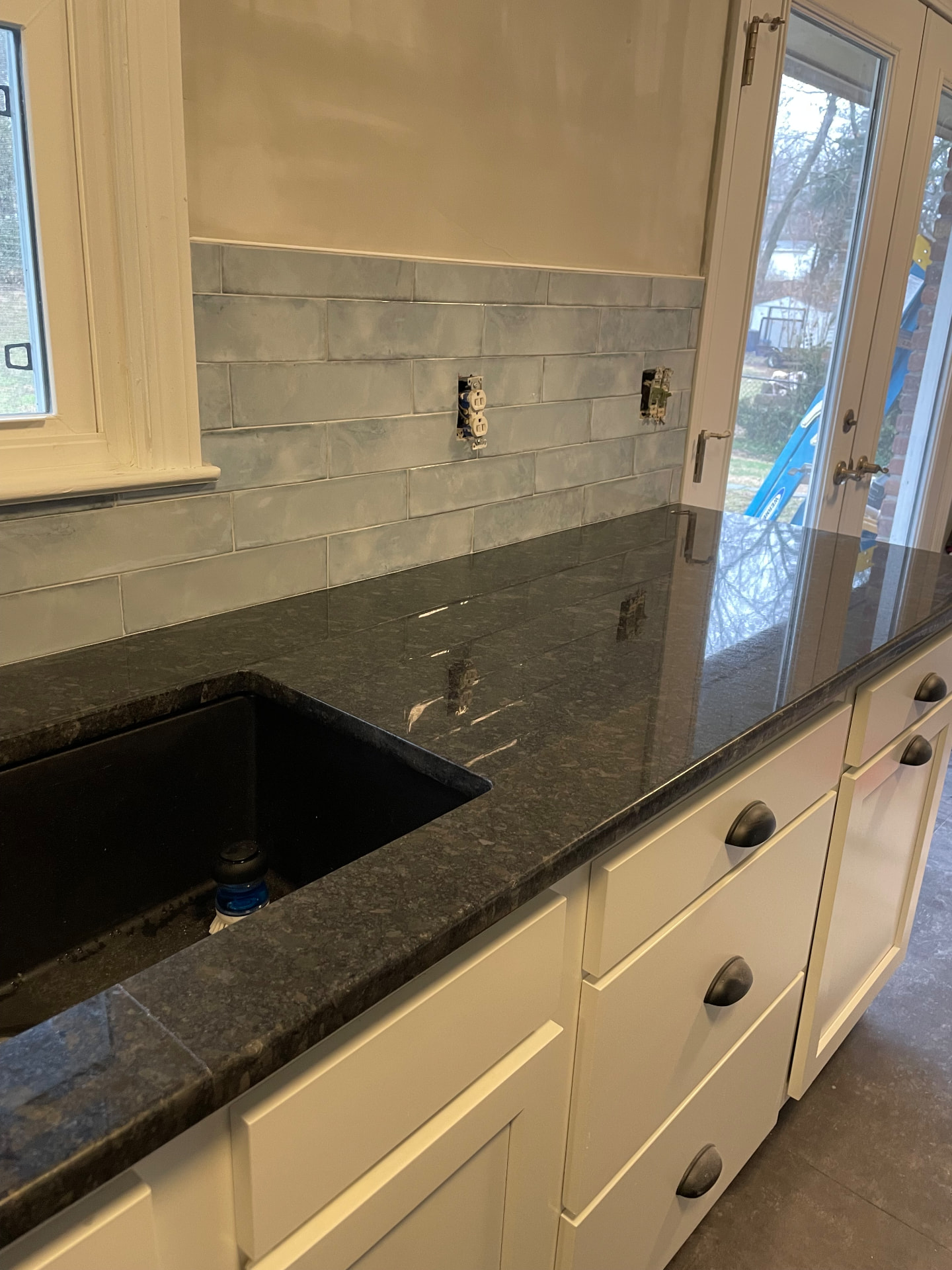 Kitchen sink run with white cabinets, dark granite-style countertops, and blue-gray subway tile backsplash in Frankfort, KY